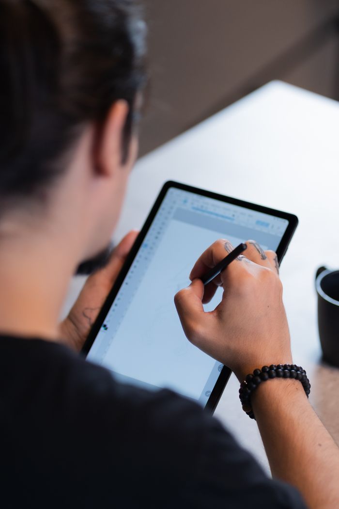 services-02 Person using a stylus to draw on a digital tablet, indoors setting.