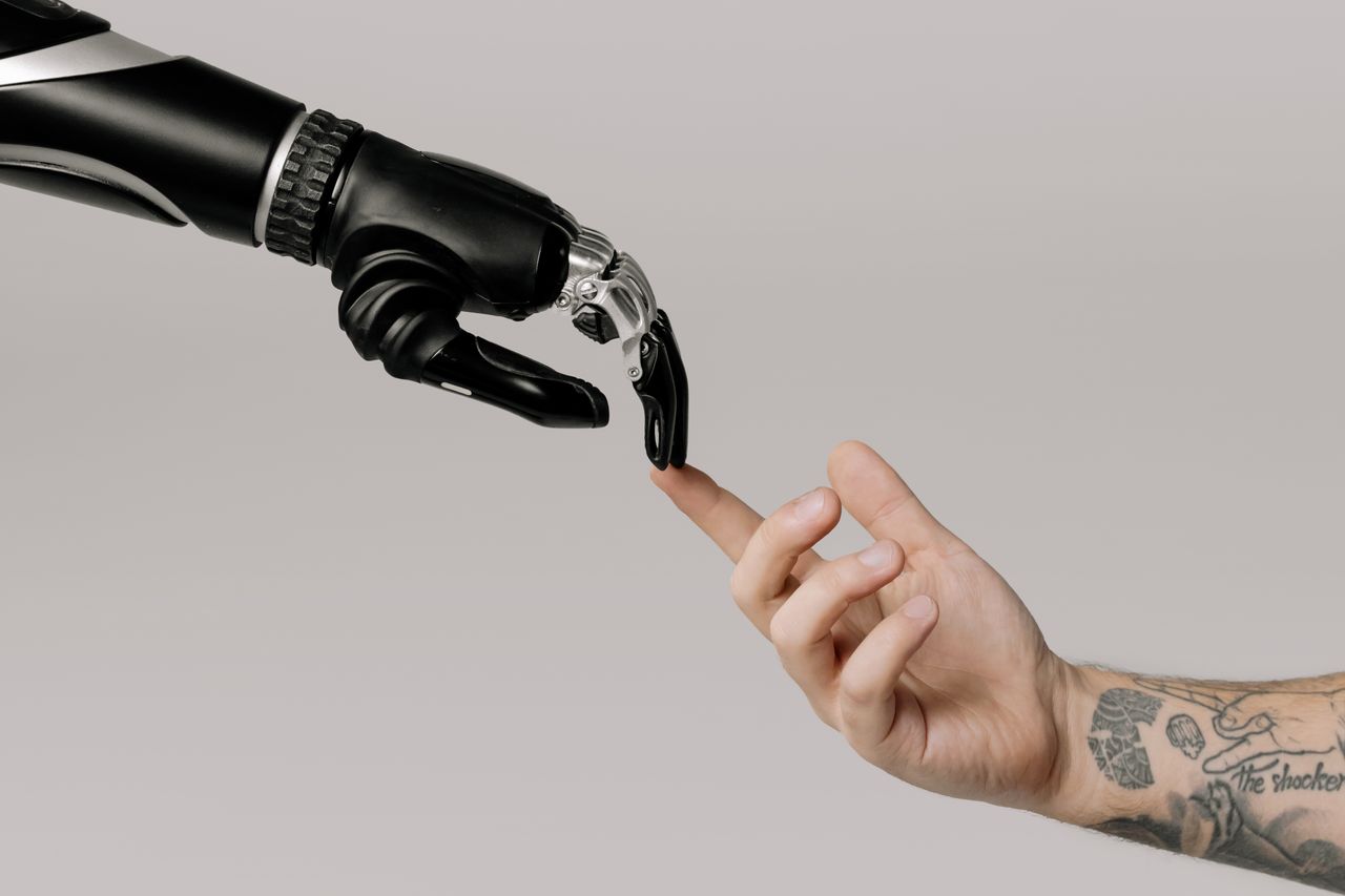 gallery-4 A human hand with tattoos reaching out to a robotic hand on a white background.