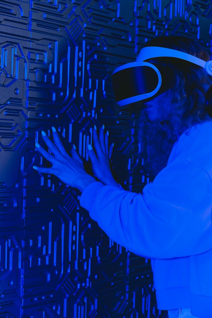 gallery-1 A woman with a VR headset interacts with a textured wall under blue lighting.